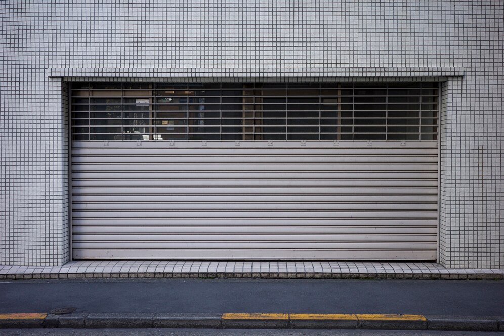 Minimalist storefront with a metallic rolling shutter and grid pattern, set against a tiled wall.
