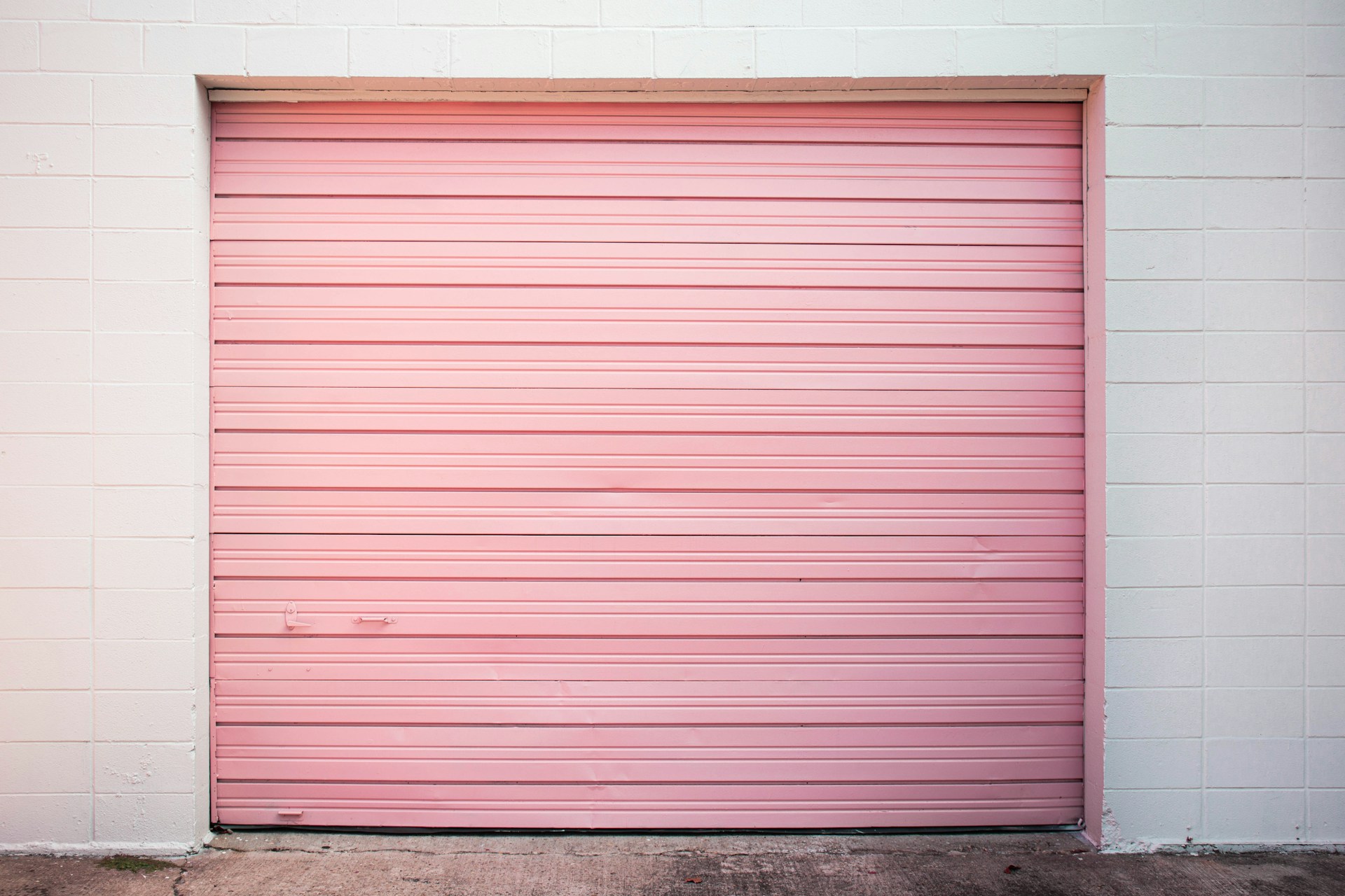 Pink garage door against a white wall, featuring horizontal slats and a simple, modern design. Perfect for trendy aesthetics.