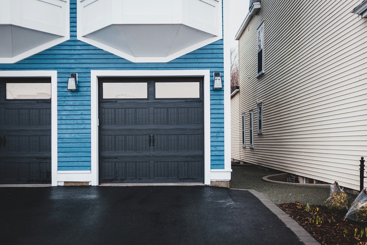 Modern blue house exterior with a dark garage door and side yard view. Stylish architecture and clean driveway.