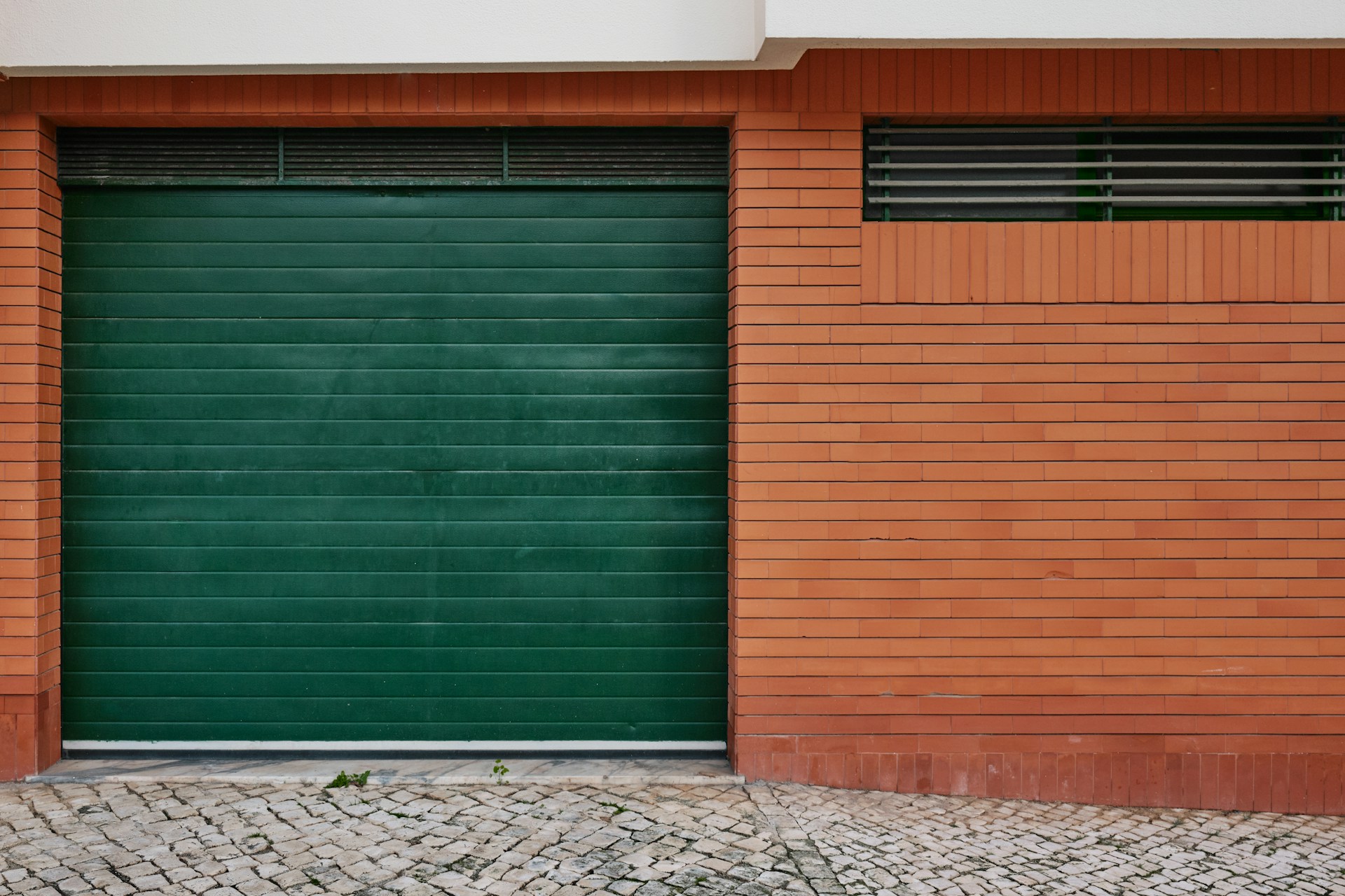 Green garage door with a brick wall background, featuring a subtle texture and minimalist design.