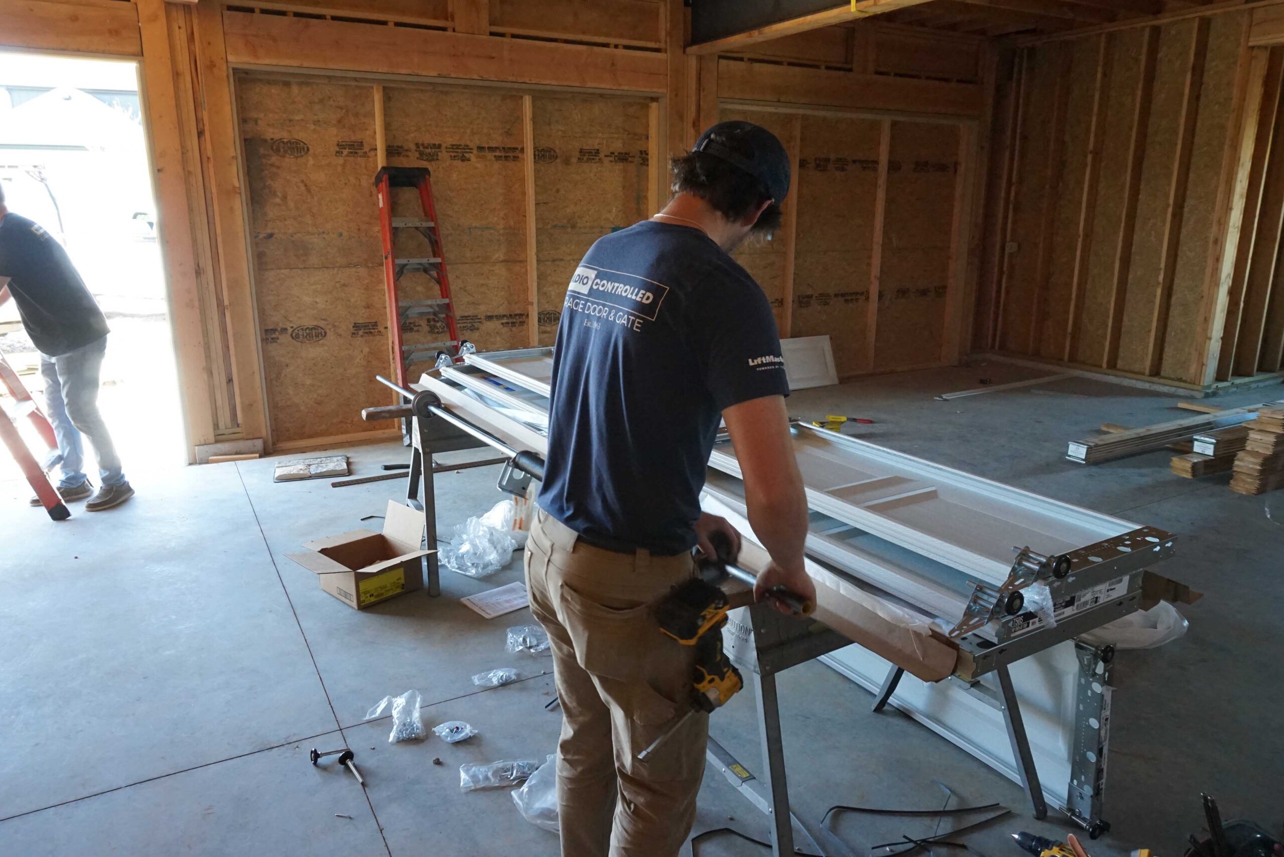 Construction worker assembling a sliding door in a framed home interior, with tools and materials scattered around.
