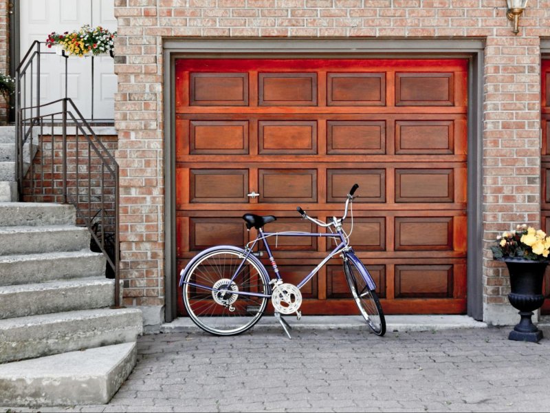 Charming blue bicycle parked next to an elegant wooden garage door, framed by a stone walkway and potted flowers.