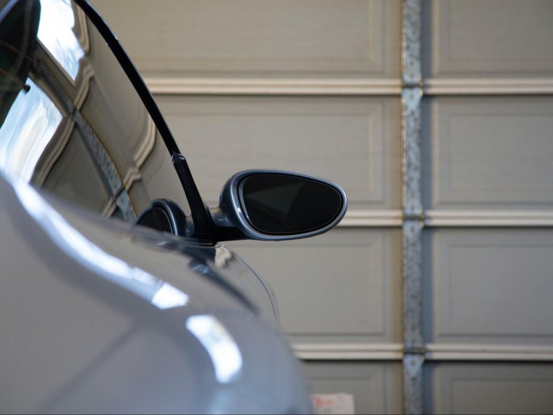 Close-up of a car's side mirror reflecting light, against a backdrop of a garage door. Ideal for automotive enthusiasts.