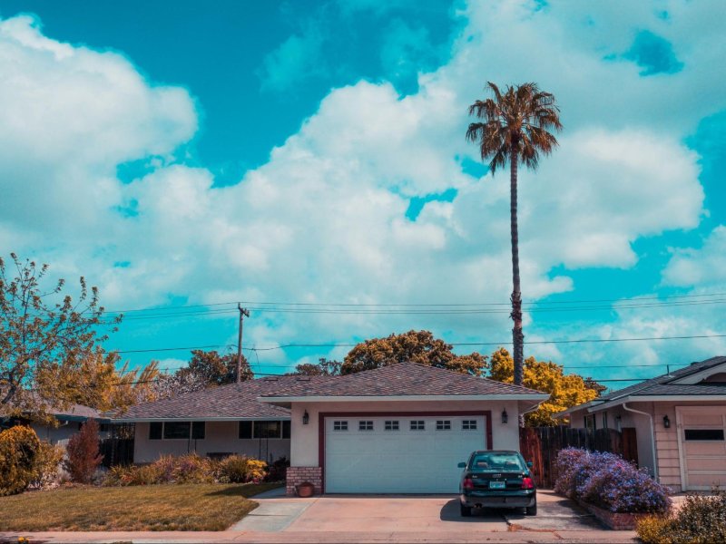 Modern suburban home with a palm tree, bright blue sky, and puffy white clouds in the background.