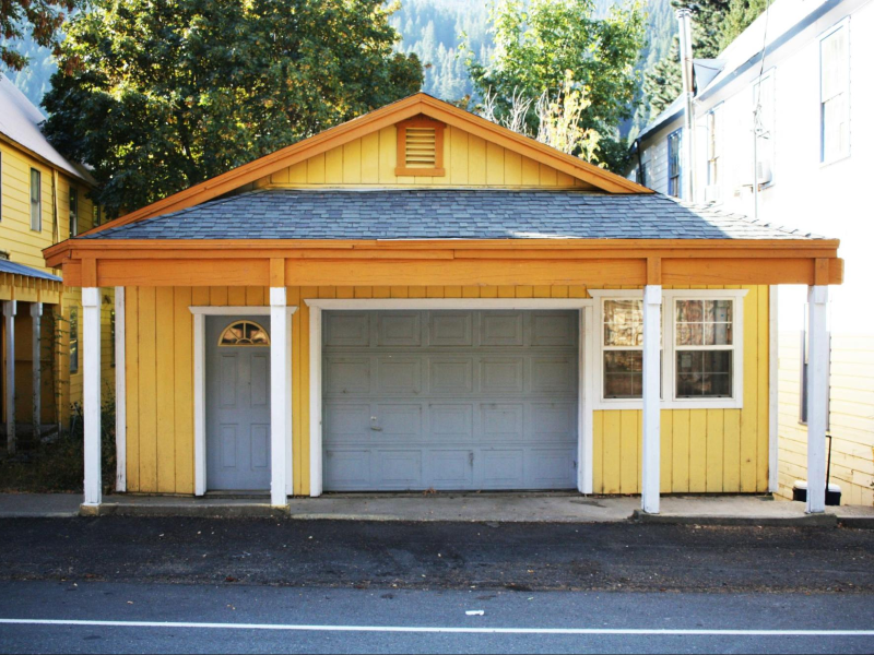 Charming yellow house with a garage and front porch, nestled among trees in a quaint neighborhood. Perfect for cozy living.