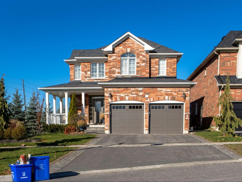 Beautiful brick house with two garage doors, surrounded by greenery and a blue recycling bin in the driveway.