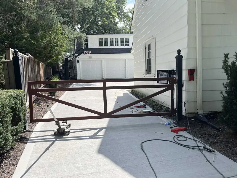 Automatic gate installation in a residential driveway, showcasing a large iron gate and surrounding greenery.