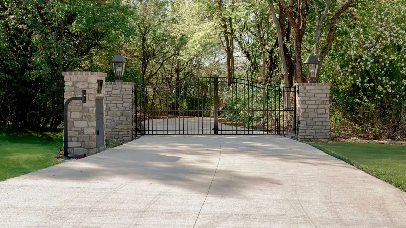 Black wrought iron gate with stone pillars featuring gate opener installation replacement for automated entry and security.