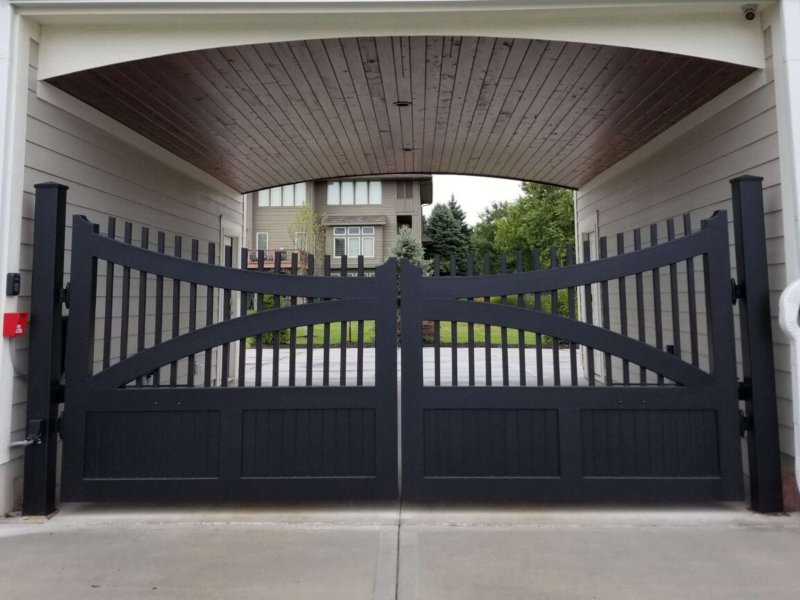 Elegant black wooden driveway gate with intricate design, framed by a covered entrance to a modern home.