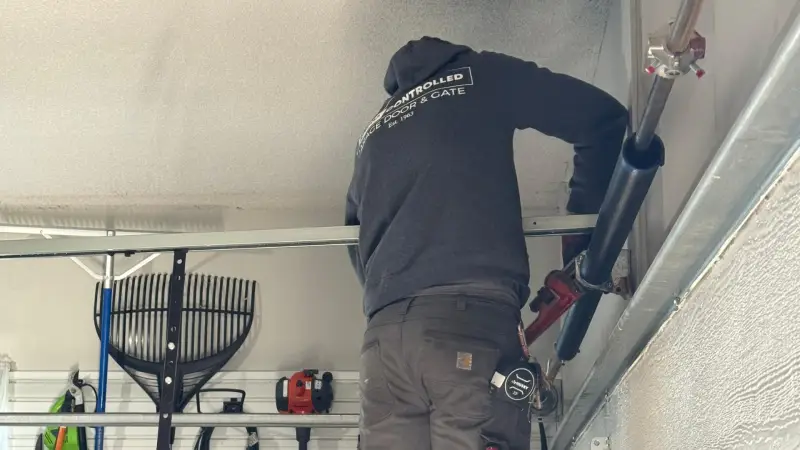 A technician installs a ceiling-mounted garage door system, with tools and equipment visible in the background.