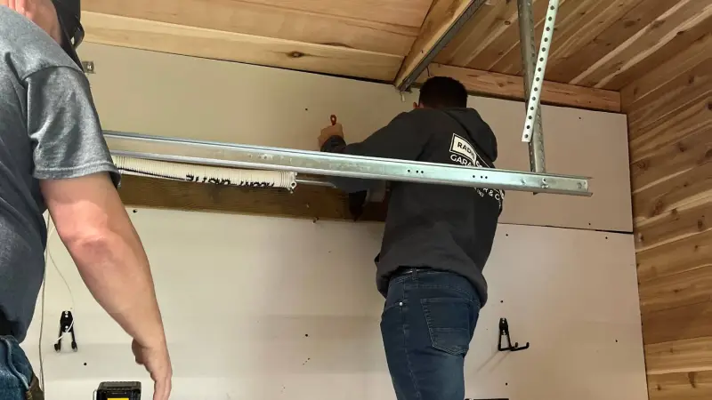 Two individuals installing a wall panel in a garage, using tools and equipment for home improvement.