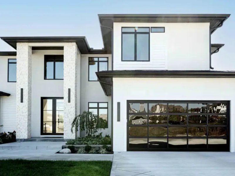 Modern two-story home with sleek design, large windows, and elegant stone accents, showcasing a stylish garage door.