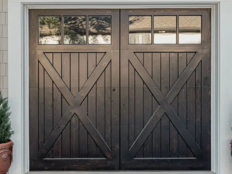 Double barn doors with glass panels, framed by greenery and a stylish exterior, adding rustic charm to the entrance.