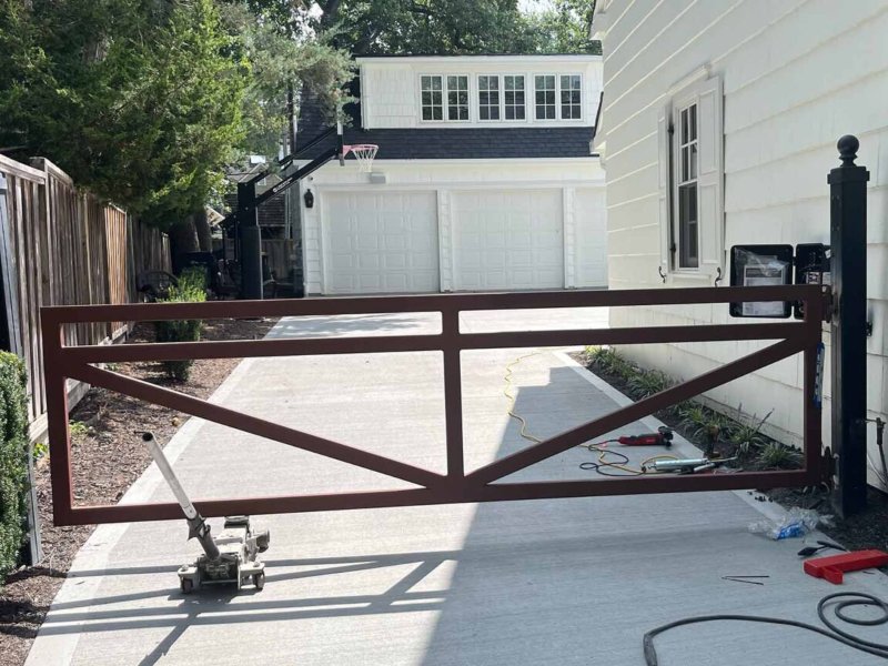 Modern driveway gate with a rustic design, opening to a clean driveway and a two-car garage in a residential setting.