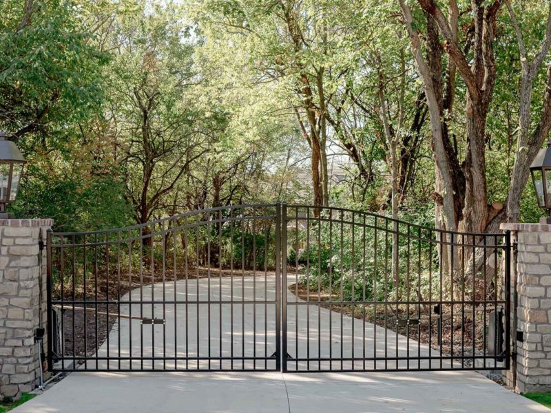 Elegant black wrought iron gate opening to a serene, tree-lined driveway, inviting you to explore the lush surroundings.