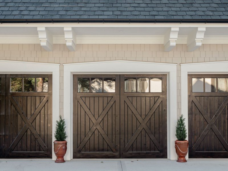 Three dark wood carriage-style garage doors with white trim, showcasing durable materials for long-lasting curb appeal.
