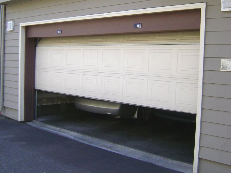 A crooked white garage door stuck halfway open, illustrating the need for immediate garage door repair.