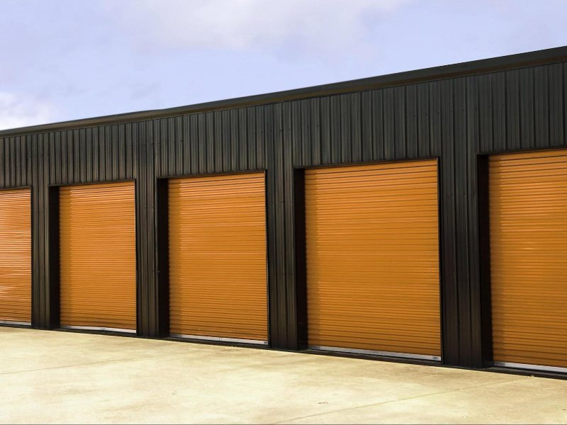 Row of orange roll-up doors on a black commercial facility, highlighting the value of regular garage door maintenance.
