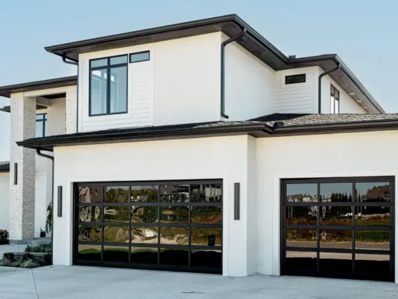 Modern white house with glass garage doors and gutters, key areas for maintenance to prevent expensive home repairs.