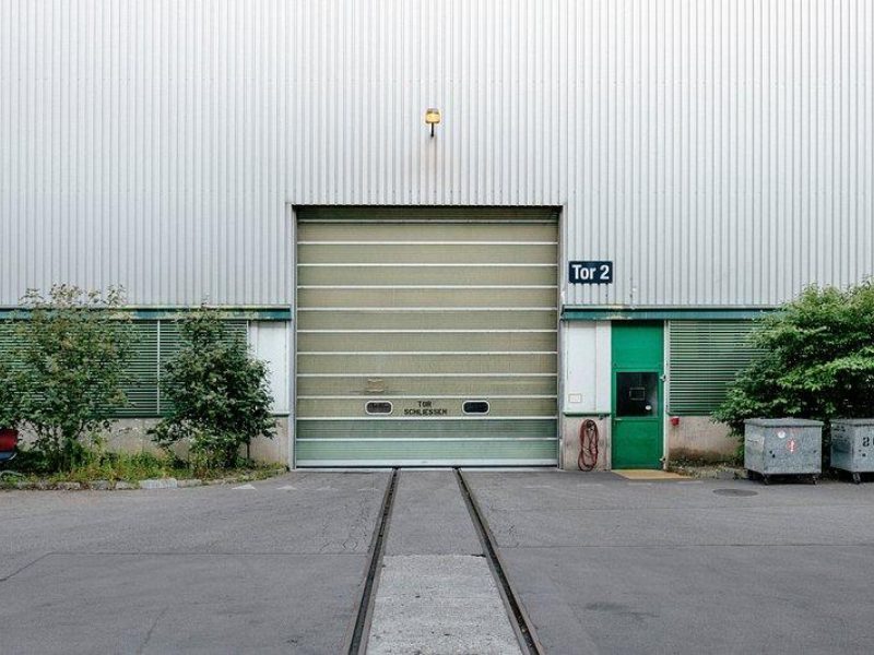 Industrial roll-up garage door labeled Tor 2, demonstrating safety and compliance features for commercial buildings.