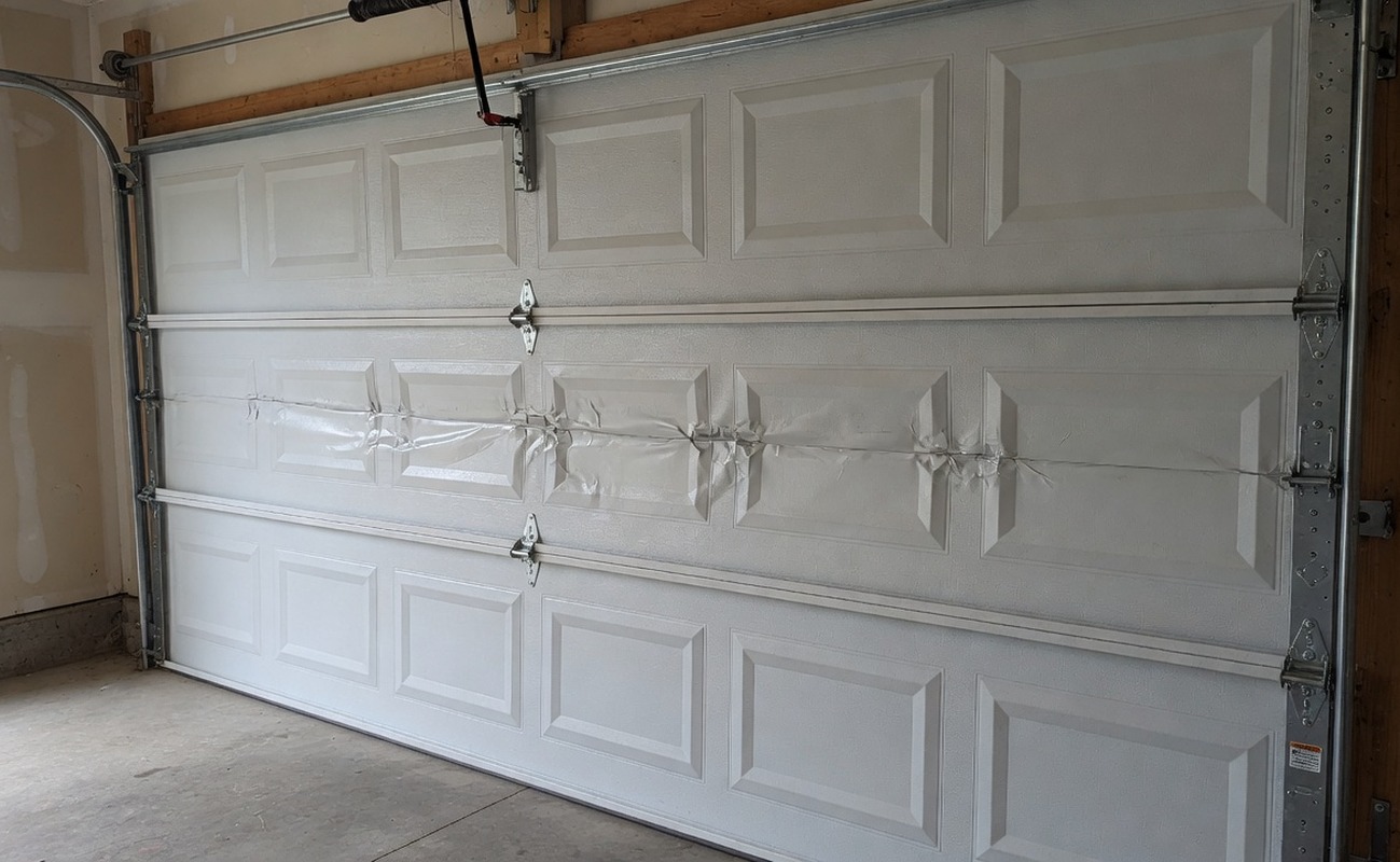 Damaged white garage door with visible dents and creases, highlighting the need for gar panel repair or replacement options.